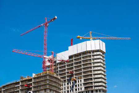 Construction cranes on the construction site of a concrete apartment building. The building and...