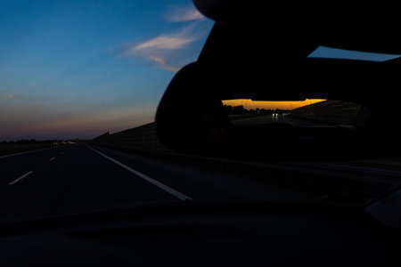 View in the outside rearview mirror of a car. View from inside of the car. Evening car ride on the...