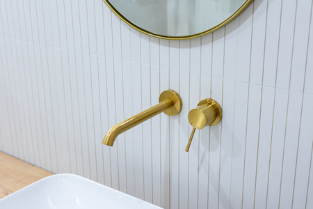 Bronze bathroom water tap in a bathroom finished with white tiles. Minimalist bathroom finish. Photographed in natural light.の写真素材