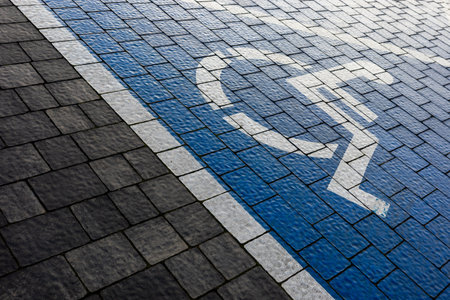 White and blue marking of a disabled parking space in a parking lot made of gray blocks. A drawing of a wheelchair painted on the surface.の写真素材