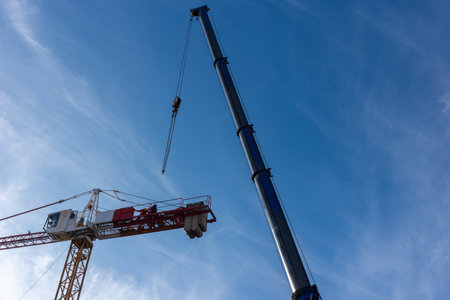 Construction of a construction crane using a mobile crane. Daytime shot of both machines against a...