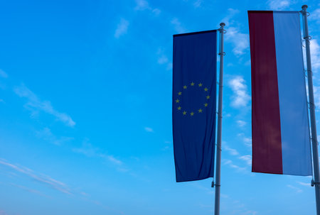Polish and European flags flying on a mast against a blue sky background. Photo taken in the late afternoon, natural lightの写真素材
