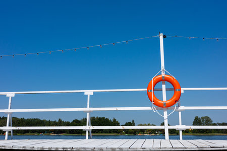Orange swimming rescue wheel hung on the rails of the white jetty. Safety equipment on the water bankの写真素材