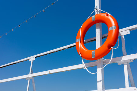 Orange swimming rescue wheel hung on the rails of the white jetty. Safety equipment on the water bankの写真素材