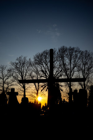 Silhouette of a cemetery cross against the orange sunset sky. Photo taken in autumn, just before evening.の写真素材