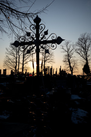 Silhouette of a cemetery cross against the orange sunset sky. Photo taken in autumn, just before...
