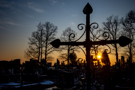 Silhouette of a cemetery cross against the orange sunset sky. Photo taken in autumn, just before evening.の写真素材