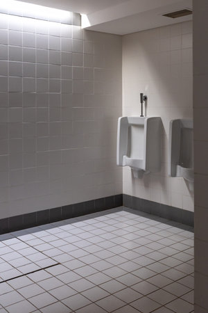 White urinals in the men's public restroom. The restroom walls are lined with white tiles, and the floor is white tiled.の写真素材