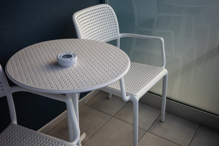 A round, white object on a plastic balcony table. Gray plastic chairs next to the table.