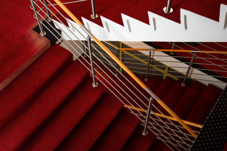 The hotel's staircase is lined with red carpeting. The carpet has been trampled by hotel guests.