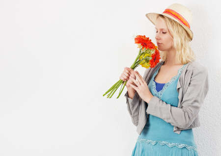 Blond pretty woman with sun hat smelling a bouquet of flowers の写真素材