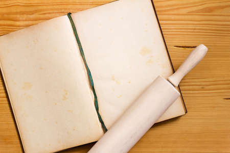 Opened yellowed cookbook with blank pages and rolling pin on wooden background - cooking still life with copy spaceの写真素材