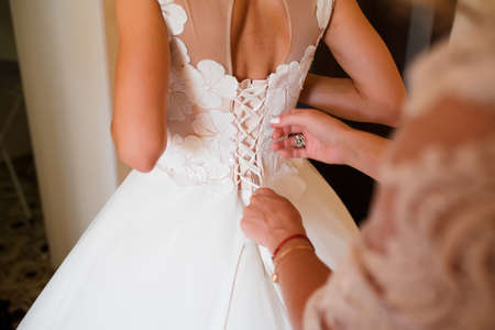 The bridesmaid helps the bride to button up the white wedding dress. Mother's hands and buttons on...