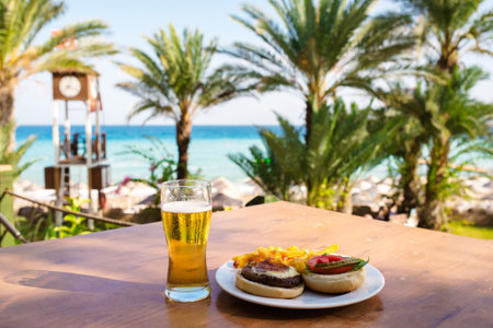 A glass of beer and a burger on a wooden table against the seaの写真素材