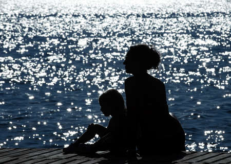 Profiles of mothers and daughters against the glittering seaの写真素材
