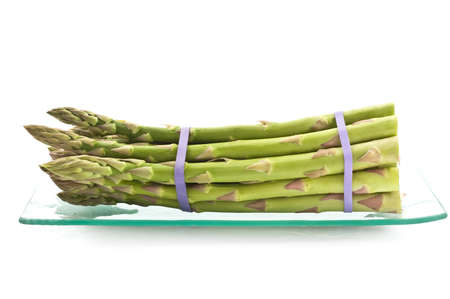 Bunch of fresh asparagus on glass plate isolated on white backgroundの写真素材