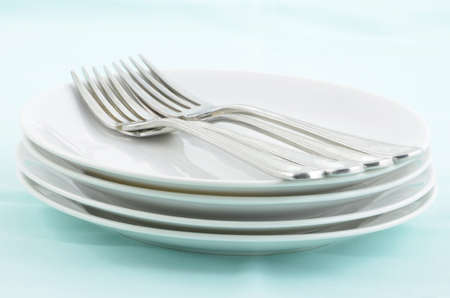 Stainless steel forks on white plates with pale aqua background