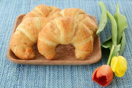 Fresh buttery croissants on rustic wooden plate on blue backgroundの写真素材