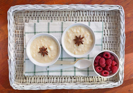 Creamy home made rice pudding with sweet juicy raspberries on wicker trayの写真素材