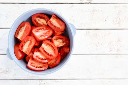 Fresh organic Roma or plum tomatoes cut in half in blue plastic bowl on weathered white board background.  Healthy eating concept.  Flat lay with room for text.の写真素材