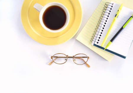 Coffee on yellow plate and notebooks with pen and pencil and eyeglasses in flat lay composition. ...