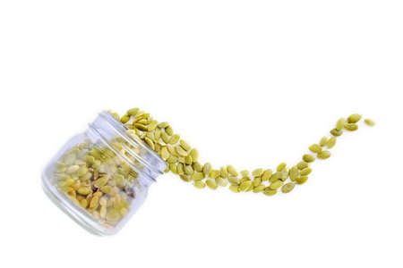 Raw organic pumpkin seeds spilling from blue jar on white background.  Shot from overhead in flat lay composition with copy space. Healthy snack concept.の写真素材