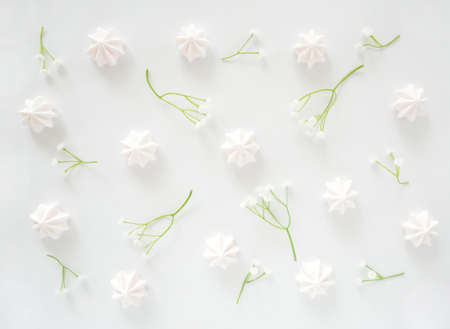 Delicate pale pink meringue candy kisses with little white flowers in flat lay composition as a backgroundの写真素材