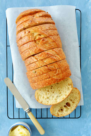 Freshly baked herb seed bread loaf in slices on blue background.  Vertical format in flay lay...
