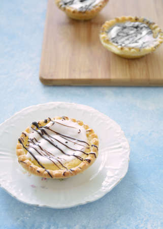 Iced almond tarts with chocolate drizzle on bamboo board and white plate in vertical format. Light...