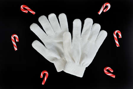 Little white knitted gloves with candy canes isolated on black background from overhead in...