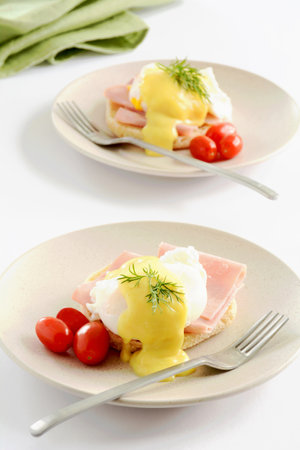 Two Eggs Benedict with cherry tomatoes on cream plates with white background in vertical format.  Healthy, nutritious breakfast or lunch.の写真素材