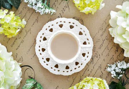 Cup of tea with artificial flowers on antique paper with script background shot from above in flat lay composition.  Springtime still life.の写真素材