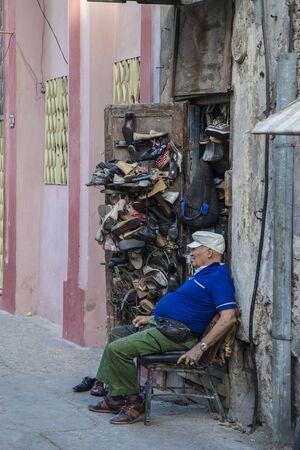 Havana, Cuba - 24 January 2013: A view of the streets of the city with cuban people. A shoemaker sits next to his shop, he repairs and sells shoes.のeditorial素材