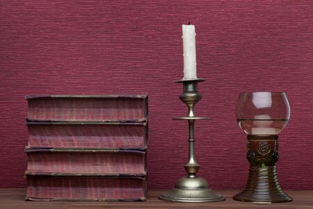 Renaissance, rummer wine glass, old books and candle holder on the burgundy background.の写真素材