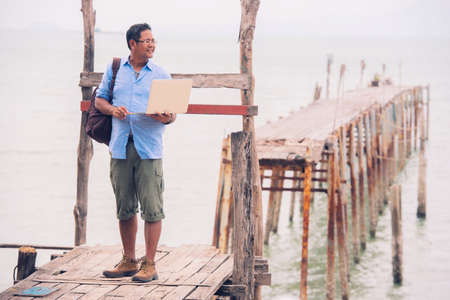 Asian male tourist standing at old wooden bridge using computerの写真素材