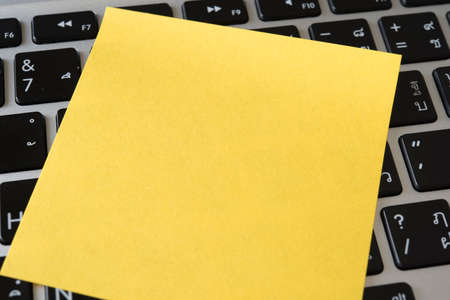blank yellow note paper with computer in background