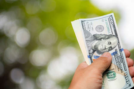 hand hold one hundred dollar bill over blur tree background