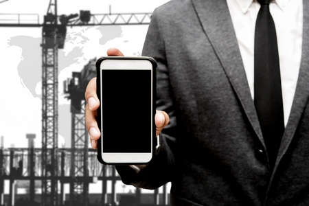 business man holding smart phone with blur image of construction craneの写真素材