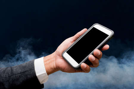 hand hold smart phone with smoke in backgroundの写真素材