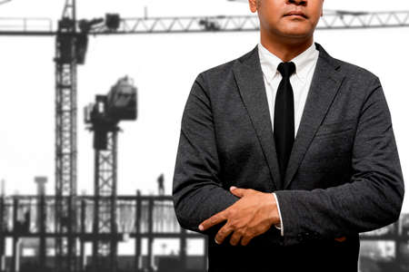 businessman standing with construction crane in backgroundの写真素材