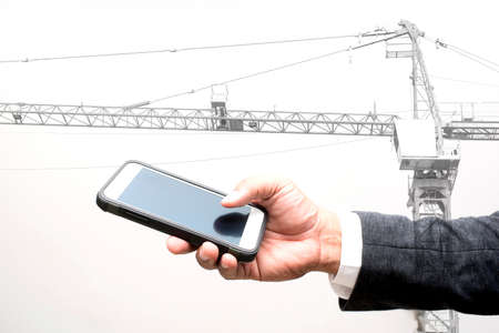 business man holding smart phone double exposure with construction craneの写真素材