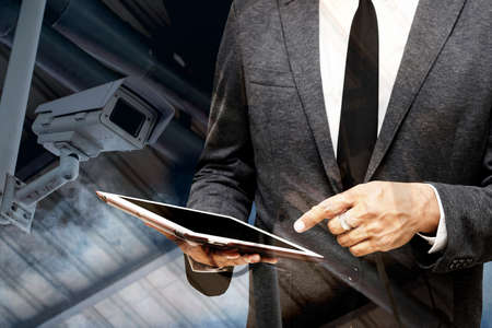 business man holding computer tablet selective focus on pointing finger with smoke picture in background double exposure with cctv cameraの写真素材