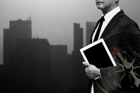 business man holding computer tablet with city light in background double exposure with compass with black and white filterの写真素材