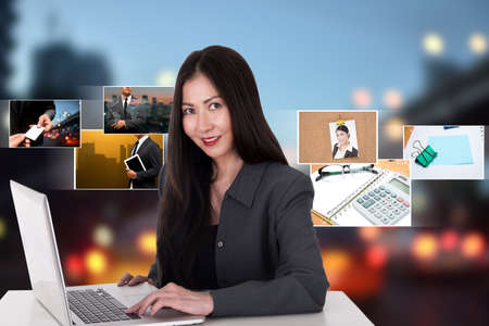 Asian woman using computer with digital photo album in backgroundの写真素材