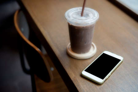 smart phone on the table with oce coffee inside coffee shopの写真素材