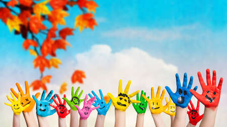 many colored hands with smileys in front of an autumnの写真素材
