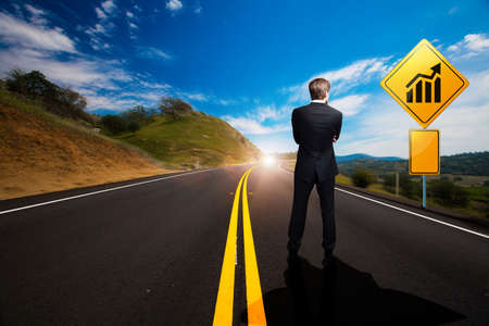 businessman standing in front of a sign with a chart on a windy roadの写真素材