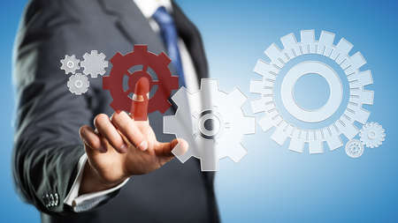 business man pressing a specific cog wheel to keep the system running 