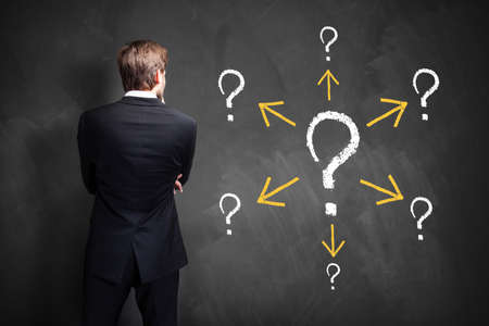 businessman stands in front of a blackboard having many questionsの写真素材