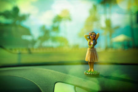 little hula dancer figure in a car with a beautiful hawaiian beach park in the background